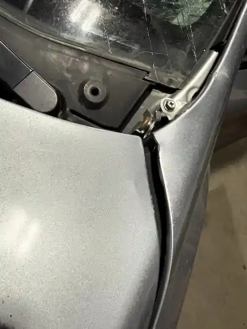 Bent cowl corner on a Subaru Impreza where the hood struck the windshield frame at highway speed.