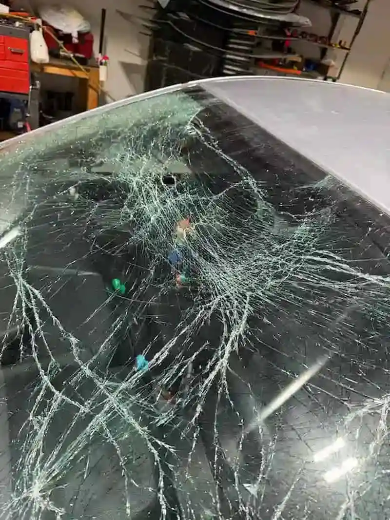 Subaru Impreza windshield completely shattered after the hood flew open at highway speed — photographed inside the 123 Glass Company shop in Omaha.