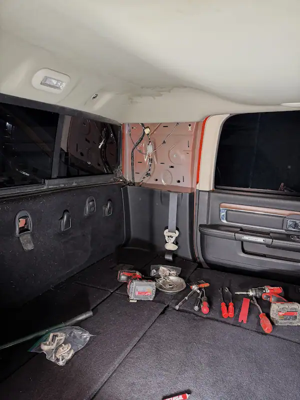 Interior of a pickup truck cab with trim panels removed on both sides, back glass visible, and diagnostic tools laid out across the rear seat area.