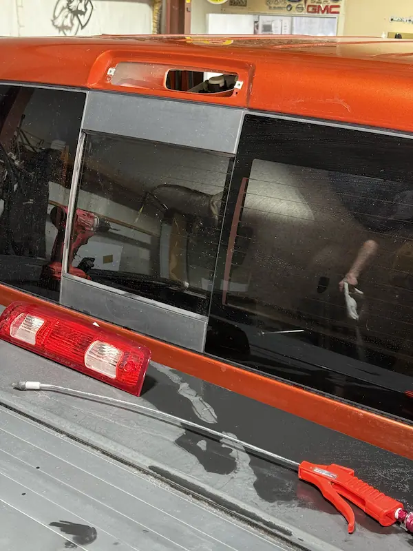 Exterior rear view of an orange pickup truck with the taillight assembly removed and sitting in the truck bed, taillight opening exposed — ready for new EPDM gasket fabrication.