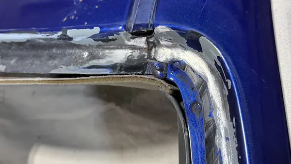 Driver side upper windshield corner during rust cleanup on a 2004 Chevy Monte Carlo — grinding in progress, not yet complete.