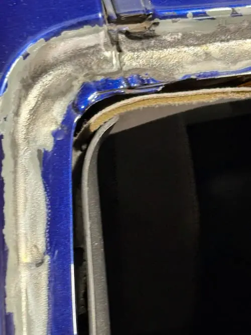 Passenger side upper windshield corner during rust cleanup on a 2004 Chevy Monte Carlo — grinding in progress, not yet complete.