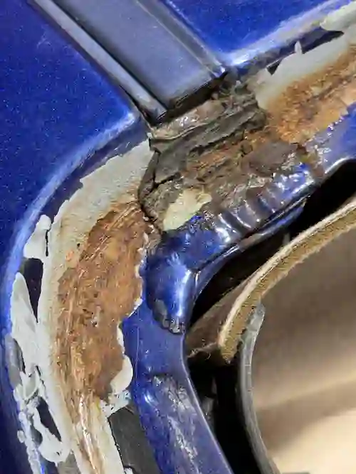 Corroded pinch weld at the passenger side upper windshield corner of a 2004 Chevy Monte Carlo — rust exposed after glass removal.