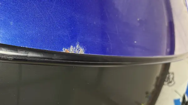 Small rust bubble visible along the windshield molding edge of a 2004 Chevy Monte Carlo — the first visible sign of corrosion at the pinch weld.