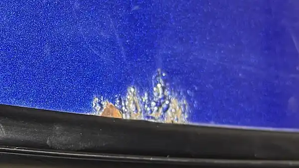 Close-up of rust bubble breaking through the paint at the windshield molding edge on a 2004 Chevy Monte Carlo.