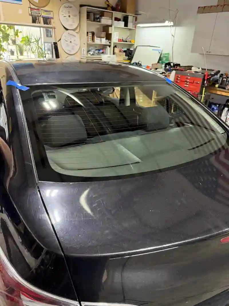 New rear glass installed on a black sedan with blue tape strips in place at 123 Glass Company in Omaha